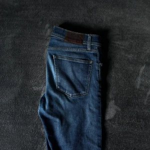 Mörkblå jeans från J Lindeberg - Snygga mörkblå jeans från J. Lindeberg med klassisk femficksdesign. Står att den är skinnyfit men passar mycket mer som slimfit. Kom privat vid funderingar. Nypris cirka 1500