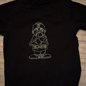 Svart t-shirt med glittrig design - Snygg svart t-shirt med en glittrig design på framsidan. Perfekt för att ge din outfit lite extra bling. T-shirten är kortärmad och är oversized.