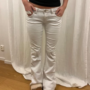 Vita bootcut jeans - Snygga vita bootcut jeans med låg midja och stilrena fickor med knappar bak. Perfekta för en avslappnad look med en touch av retro. Passar bra till både sneakers och klackar.