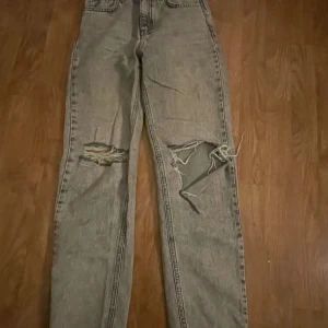 Grå jeans med slitningar - Säljer ett par grå jeans med coola slitningar på framsidan. De har en klassisk femficksdesign och en rak passform. Perfekta för en avslappnad stil. (Gina Young 146)