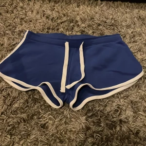 Blå shorts med vita detaljer - Snygga blå shorts med vita kanter och snörning i midjan. Perfekta för en avslappnad stil eller sportiga aktiviteter. De har en bekväm passform och är gjorda i ett mjukt material.