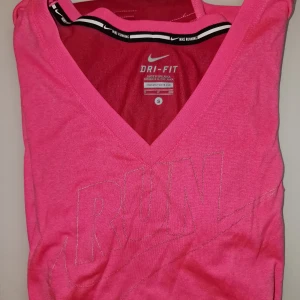Rosa Dri-Fit T-shirt från Nike - Säljer en rosa Dri-Fit T-shirt från Nike med v-ringning och korta ärmar. Perfekt för löpning med 'RUN' tryckt på framsidan. Materialet är lätt och andas bra. Garderobsrensning så kika gärna på övriga auktioner.