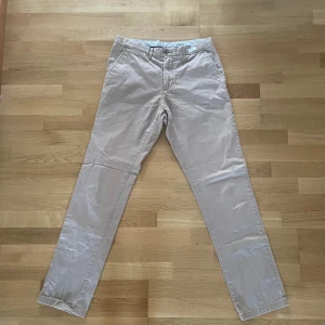 Beige chinos från Tommy Hilfiger - Säljer ett par stilrena beige chinos från Tommy Hilfiger. De har en klassisk design med knappar och dragkedja. Perfekta för en avslappnad men ändå uppklädd look.