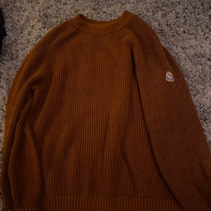 Brun stickad tröja från Moncler - Säljer en snygg brun stickad tröja från Moncler med rund hals och långa ärmar. Perfekt för kyliga dagar. Tröjan har Monclers logga på ärmen. Passar både till jeans och chinos.