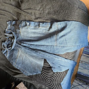 Blå jeans med stjärndetalj - Unika blå jeans med en cool svart stjärndetalj på fickan. Byxorna har en loose passform och är tillverkade i jeansmaterial. Perfekta för en avslappnad stil med en twist. Mått: längd: 107 cm, midja 80 cm, höft: 113 cm och lår 71 cm