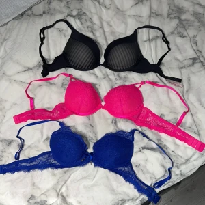 3 snygga oanvända Bh:ar - Säljer tre snygga oanvända BH:ar. En svart med transparenta ränder från Hunkemöller i storlek 65E. En rosa med spetsdetaljer och en blå med spets och liten rosett framtill, båda dem är från Newyorker i storlek 75B. En för 50kr eller alla för 100kr.