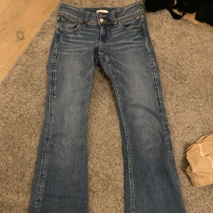 Blå bootcut jeans - Snygga blå bootcut jeans med klassisk femficksdesign och knappgylf. Perfekta för en avslappnad stil. De har en lätt tvättad look som ger en vintage känsla.