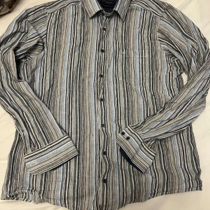 Randig skjorta från Gant - Snygg randig skjorta från Epson i olika nyanser av blått, grått och brunt. Skjortan har långa ärmar och knappar framtill. Perfekt för en stilren look.