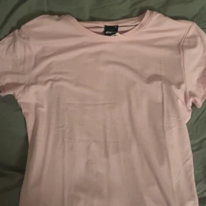 Rosa t-shirt från Gina Tricot - Säljer en mjuk rosa t-shirt från Gina Tricot. Den har en klassisk rund hals och korta ärmar, perfekt för en avslappnad stil. Passar bra till jeans eller kjol för en enkel look.