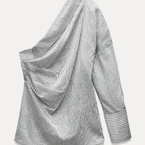 Grå- och vitrandig offshoulder-skjorta från Zara - Trendig grå- och vitrandig skjorta med en unik offshoulder-design. Skjortan har lång ärm och knappar baktill, vilket ger en stilren look. Perfekt för att sticka ut med en modern touch. Helt oanvänd med prislapp kvar!
