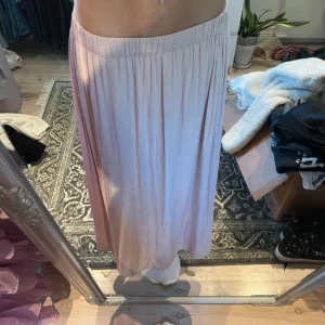 Ljusrosa långkjol från Gina Tricot - Säljer en elegant ljusrosa långkjol från Gina Tricot. Kjolen har en mjuk och flödande design med ett elastiskt midjeband för extra komfort. Perfekt för en stilren look.