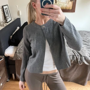 Grå kofta från Zara - Säljer en stilren grå kofta från Zara med rund halsringning och en enkel knapp framtill. Perfekt för lager-på-lager och passar till många olika outfits. Koftan har långa ärmar och är tillverkad i ett mjukt material.