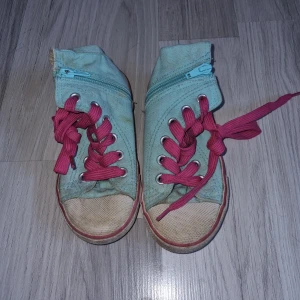 Turkosa sneakers med rosa snörning - Säljer ett par turkosa sneakers med rosa snörning och dragkedja på sidan. Skorna har en vit sula med rosa rand och en rund tå. Perfekta för en avslappnad stil.