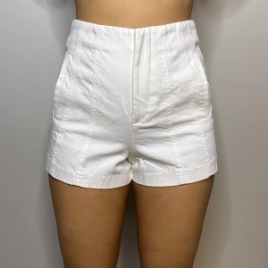 Vita shorts från Zara - Vita midjeshorts från Zara i en stilren design. De är högmidjade och tillverkade i bomull, vilket gör dem både bekväma och trendiga.