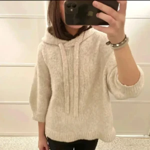 Beige stickad hoodie - Mysig beige stickad hoodie med trekvartsärm och en avslappnad passform. Perfekt för kyliga dagar med sin bekväma huva och ribbade kanter. En stilren och enkel design som passar till det mesta.