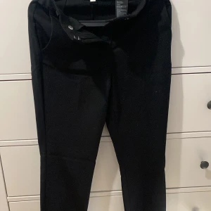 Svarta byxor - Säljer ett par svarta kostymbyxor i klassisk stil. De har en enkel design med knapp och dragkedja framtill. Perfekta för både vardag och fest! Helt oanvända, köpta för 300kr