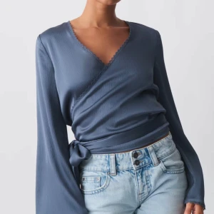 Blå omlottopp med knytband - Säljer en superfin blå omlottopp med långa ärmar och knytband i midjan. Perfekt för både vardag och fest. Den har en stilren look som passar till det mesta. Aldrig andvänd då jag har svårt att styla den. Kollar vilket intresse som finns!🩷kom med pris