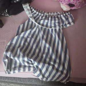 Randig offshoulder klänning från Lindex - Säljer en superfin randig offshoulder topp från Lindex i storlek 158/164. Den har ett snyggt blått och vitt mönster och är perfekt för sommardagar. Toppen är i bra skick och har en bekväm passform. Perfekt för både vardag och fest! 🌟