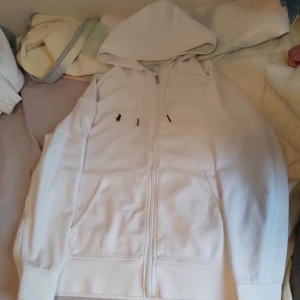 Vit Ralph Lauren Zip Hoodie - Polo Ralph Lauren kofta. Storlek M/175. Ser ut som på bilden med den lilla pricken nära fickan. Bra skick, pris kan diskuteras.