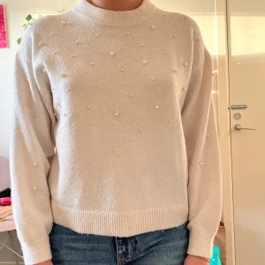 Vit tröja med pärlor - Säljer en superfin vit tröja med pärlor som dekoration. Den är perfekt för både vardag och festliga tillfällen. Tröjan har långa ärmar och en bekväm passform. Perfekt för att hålla sig varm och stilren under kyligare dagar!