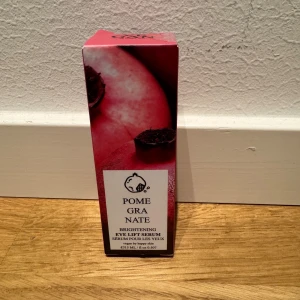 Brightening Eye Lift Serum med Granatäpple - Säljer ett Brightening Eye Lift Serum med granatäpple. Förpackningen är snyggt designad med en bild av ett granatäpple och text i svart och vitt. Perfekt för att ge dina ögon en uppfräschning och lyster. Innehåller 15 ml.