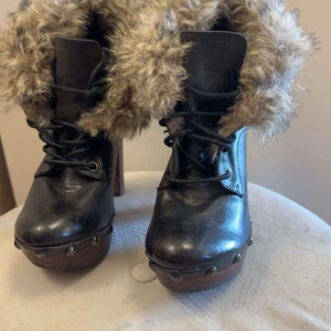 Svarta boots med pälsdetaljer - Säljer ett par snygga svarta boots från Soretti. De har en hög klack och är dekorerade med päls runt skaftet. Skorna har snörning framtill och nitar längs sulan för en extra cool look. Perfekta för höst och vinter!