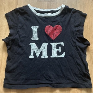 Svart topp med tryck från H&M Divided - Slutsåld svart croppad topp med tryck från H&M. Har en vit ribbad kant vid halsen och är ärmlös. Sparsamt använd + inga defekter! 🖤