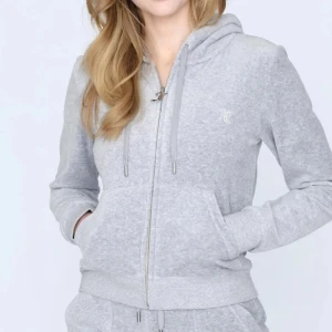 Grå juicy couture kofta - Säljer denna juicy kofta då den inte längre kommer till andvändning. Andvänd ett par gånger men fortfarande i ganska bra skick, dock har en av metall grejerna gått av från en av snörena anars bra. Strl. M