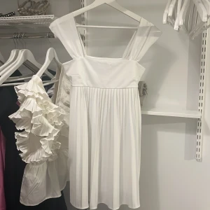 Vit klänning från Gina Tricot - Superfin vit klänning från Gina Tricot i storlek S. Den har breda axelband och en luftig passform som gör den perfekt för sommarens alla fester. Klänningen är kort och har en söt, veckad kjol som ger en härlig rörelse. 