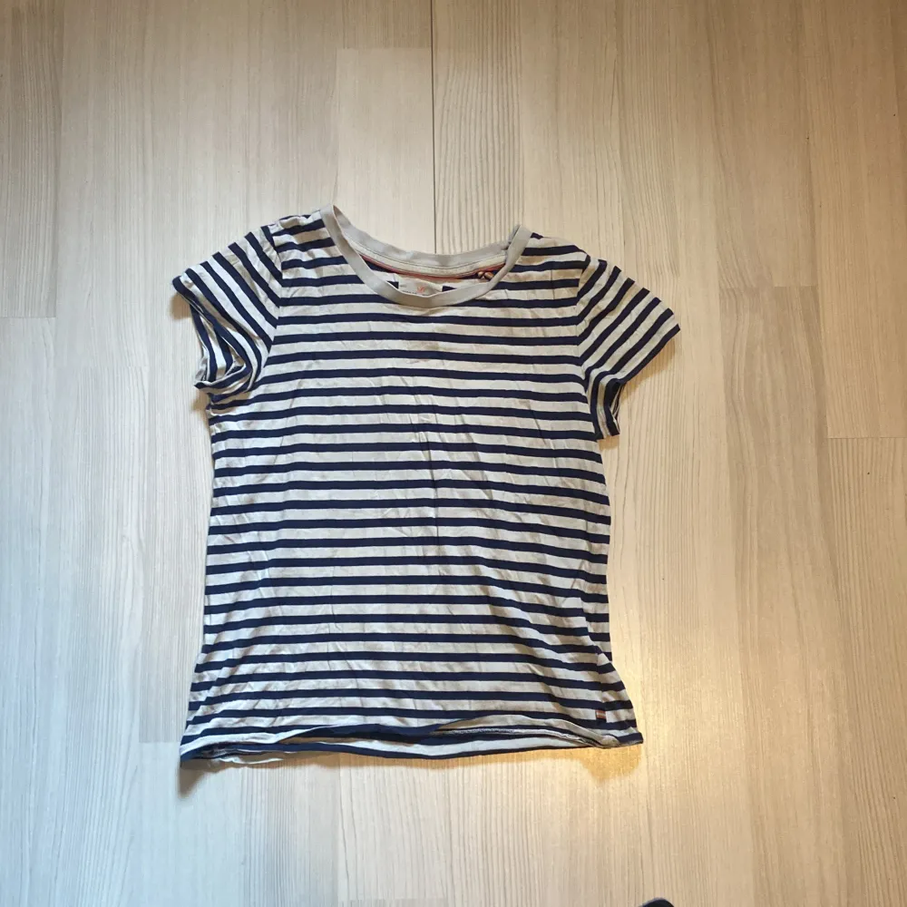 Säljer en snygg randig t-shirt från Holly & Whyte. Den är i en klassisk marinblå och vit färgkombination med korta ärmar. Perfekt för en avslappnad stil och passar till både jeans och shorts. Skön och lätt att bära!. T-shirts.