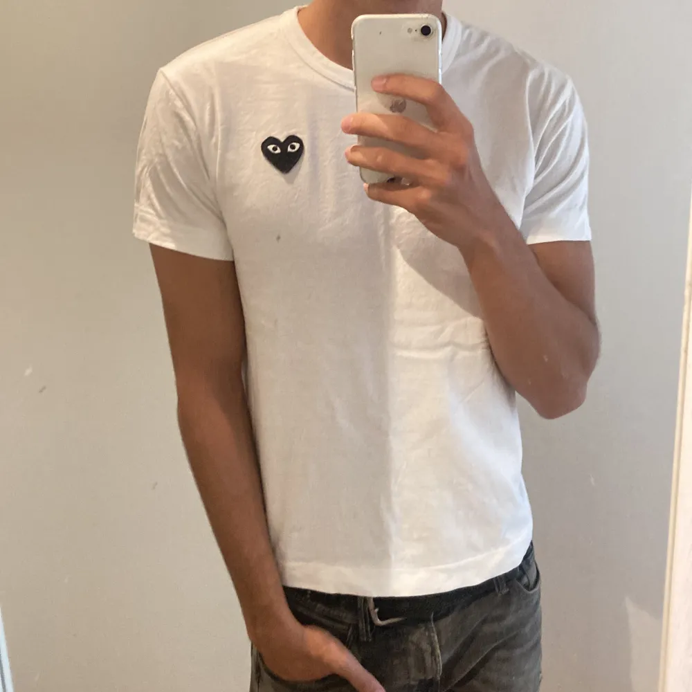 Säljer en stilren vit t-shirt från Comme des Garçons PLAY. Sprillans ny köpt denna sommar. Den har ett ikoniskt hjärta med ögon på bröstet. T-shirten är i storlek S och är gjord av 100% bomull, vilket gör den superbekväm. Perfekt för en casual look eller att styla upp med en snygg jacka. Tillverkad och köpt i Japan.. T-shirts.