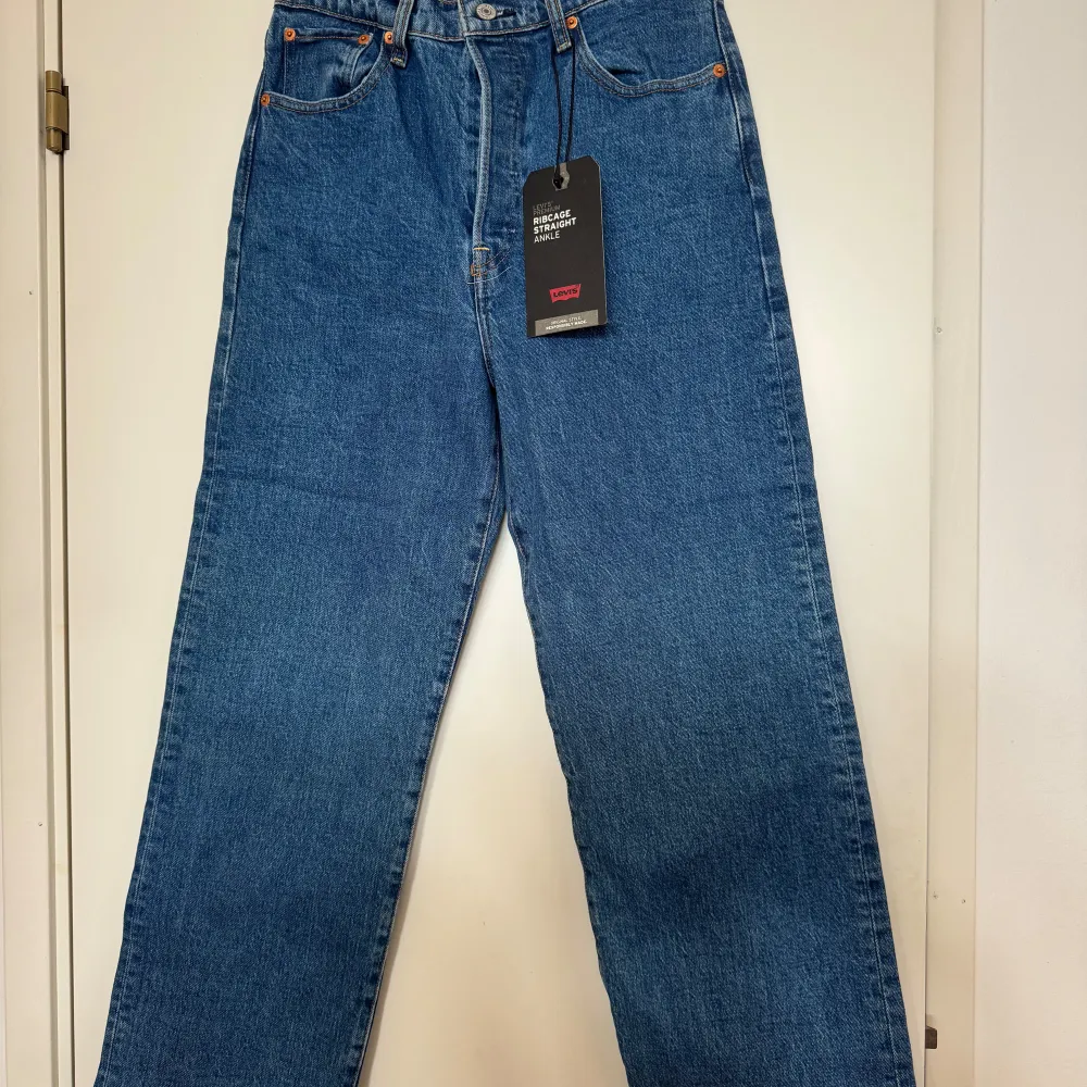 Säljer ett par snygga Levi's Ribcage Straight Ankle jeans i klassisk blå denim. De är högmidjade och har en rak passform som slutar vid ankeln. Perfekta för en avslappnad men stilren look. Jeansen har de ikoniska Levi's-detaljerna med knappar och etikett baktill. aldrig använda!. Jeans & Byxor.