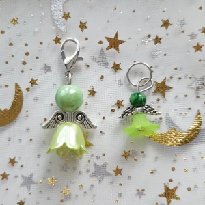 Gröna ängelberlocker med pärlor - Säljer två supersöta ängelberlocker i grönt och silver. De har en grön pärla som huvud och en blomformad kjol i ljusgrönt. Vingarna är i silverfärg och ger en magisk touch. Perfekta att fästa på ett armband eller halsband för en personlig stil!