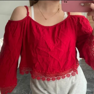 Röd offshoulder topp med spetsdetaljer - Säljer en superfin röd offshoulder topp med spetsdetaljer längst ner. Toppen har trekvartsärmar och är perfekt för sommarens fester. Den är croppad och har en lös passform som gör den både bekväm och snygg.