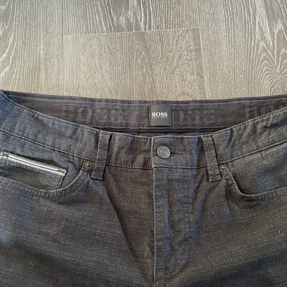 Säljer ett par snygga svarta med lite vitt mönster (se sista bild) chinos från HUGO BOSS. De är i storlek 34/30 och har en stretchig passform för extra komfort. Byxorna har en klassisk design med dragkedja och knapp framtill. Perfekta för både vardag och fest!. Jeans & Byxor.