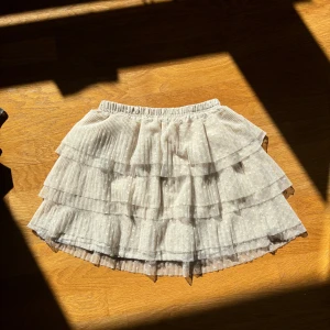 Tyll och volangkjol - Vit/cremefärgad volangkjol eller tyllkjol med prickar. Resår i midjan och underkjol så den är inte genomskinlig. Storlek 38 på lappen Midjemått: 31 - 48 cm Längd: ca 35-36 cm