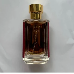 Prada parfym med röd och guld design - Säljer en lyxig parfym från Prada. Flaskan har en elegant design med en djup röd färg på sidorna och en gyllene kork. Parfymen har en klar glasflaska som visar den gyllene vätskan inuti. Perfekt för den som vill ha en exklusiv doftupplevelse. 25 ml 