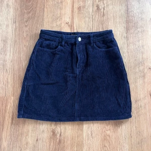 Mörkblå manchesterkjol i storlek M - Säljer en superfin mörkblå manchesterkjol i storlek M. Kjolen är gjord av 100% bomull och har en klassisk A-linjeform. Den har två fickor fram och två bak, samt en knapp och dragkedja framtill. Perfekt för höst och vinter, och kan lätt stylas med en mysig tröja eller en snygg blus. 🦋