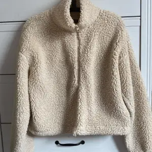 Mysig beige teddyjacka/kofta från Bik Bok i storlek XS. Perfekt för kyliga dagar med sin fluffiga och varma design. Jackan har en dragkedja framtill och långa ärmar. Den är i nyskick och redo att bli din nya favorit i garderoben!