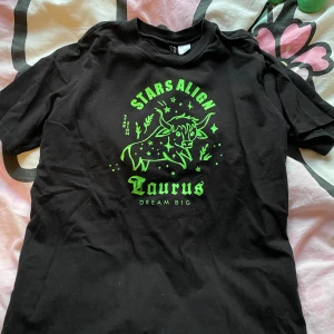 T-shirt taurus star sign svart neon grön  - Säljer denna fina T-shirt med Taurus märke på. köpt ifrån hm. Tömmer min garderob med kläder jag knappt använder/ aldrig använt 🥲 nästan allt är thriftat. Om ni har några frågor skicka gärna ett dm :) jag kan också samfrakta