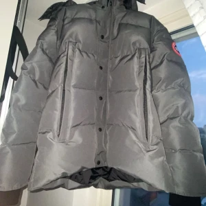Grå dunjacka med huva - Säljer en grå dunjacka från Canada goose med rödlogga, köpte för 2500 kr, måste få bort den så säljer för 1700, pris kan diskuteras, har påse och päls till den. Helt ny aldrig andvänts 