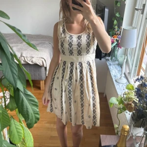 Beige ärmlös klänning med mönster - Säljer en beige klänning med svart mönster. Den är ärmlös och har knytning i ryggen.