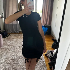 Svart kortklänning med knyt - Säljer en snygg svart kortklänning som är perfekt för fest! Den har en tight passform och korta ärmar. Klänningen har knyt på sidorna som ger en cool detalj. Perfekt för en utekväll eller en speciell tillställning. 🖤