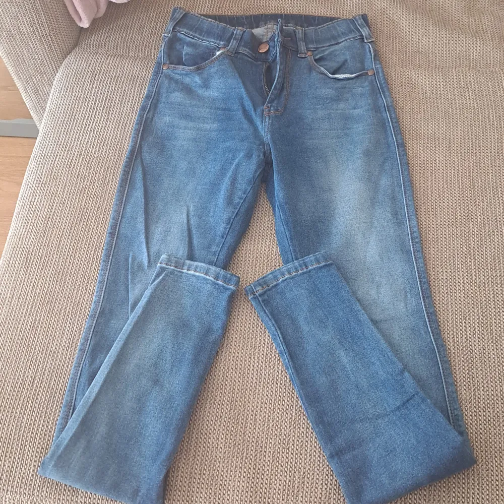 Säljer ett par snygga blå jeans med hög midja. De har en klassisk femficksdesign och en knapp- och dragkedjestängning framtill. Perfekt för vardag !. Jeans & Byxor.