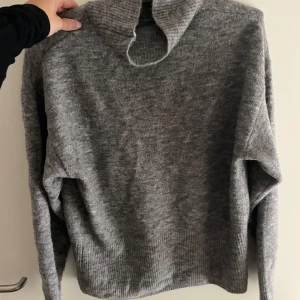 Grå stickad tröja med hög krage - Säljer en supermysig grå stickad tröja med hög krage. Perfekt för kyliga dagar! Den har långa ärmar och en ribbad kant vid ärmslut och nederkant. Passar både till vardags och lite finare tillfällen. 🧶