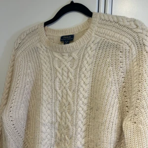 Kabelstickad Polo Ralph Lauren tröja - Benvit lite tjockare kabelstickad tröja från Polo Ralph Lauren. Använd sparsamt men lite noppror som nog lätt går bort! Den är storlek XL barn alltså 16 år, men skulle säga att den sitter som en XS-S vuxen.