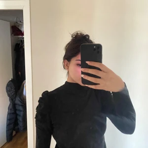 Svart långärmad tröja från Mango - Säljer en stilren svart långärmad tröja från newyorker . Den har en hög krage och puffiga axlar som ger en trendig look. Perfekt för både vardag och fest!