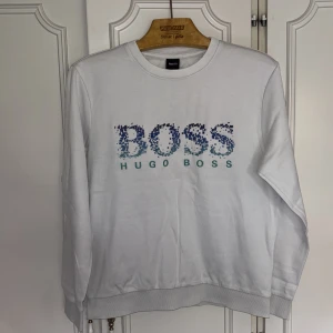 Hugo Boss tröja  - Storlek M. Mycket bra skick. Vit Hugo boss tröja med broderat tryck i blåt och grönt. Nypris: 1299kr
