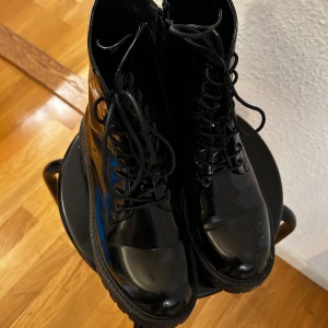 Svarta blanka kängor med snörning - Säljer ett par svarta blanka kängor i bra skick. De har en robust sula och klassisk snörning framtill. Perfekta för höst, och ger en cool look till vilken outfit som helst. Passar både till vardags och lite festligare tillfällen. Små 40!