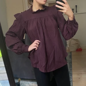 Plisserad blus från CW - Vinröd/lila blus från CW. Aldrig använd så nyskick. Det är fina detaljer på axlar och även kragen är fin med knappar.